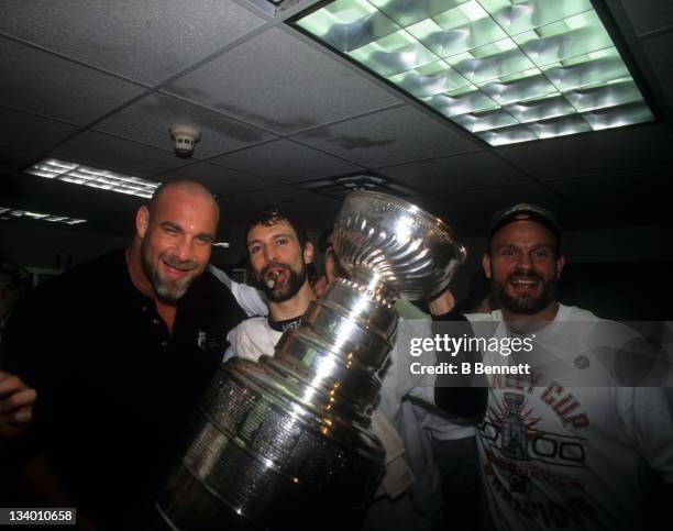 Scott Niedermayer of the New Jersey Devils celebrates in the locker room with the Stanley Cup Trophy with his teammate Ken Daneyko and wrestler Bill...