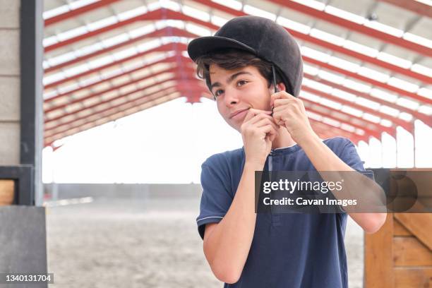 teenage boy putting a riding helmet on his head. - jockey foto e immagini stock