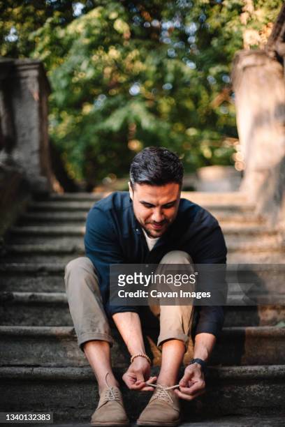 happy man tying shoelace sitting on steps in city in summer - shoelace stock pictures, royalty-free photos & images