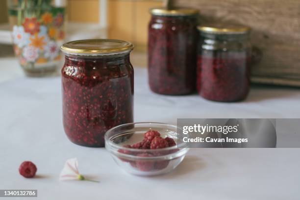 three glass jars of red raspberry jam and plate of raspberries - raspberry jam stock pictures, royalty-free photos & images