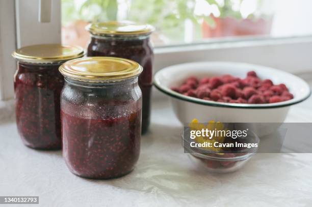 glass jars of raspberry jam and bowl of red raspberries - heliopsis stock pictures, royalty-free photos & images