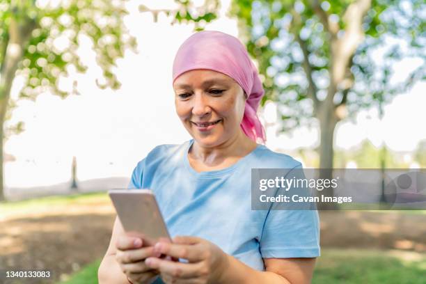 woman with cancer scarf using her smartphone - cellphone cancer illness stock-fotos und bilder