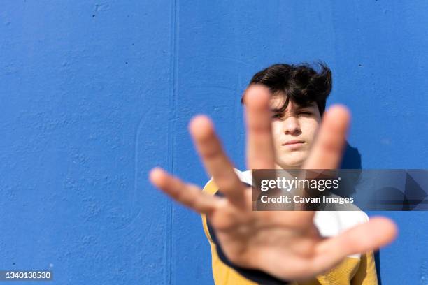 young male leaning on blue wall hiding his face under blurred hand - spain teen face bildbanksfoton och bilder