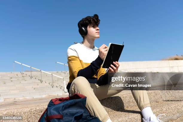 young male writing notes in a notebook sitting on a staircase - student journalist stock pictures, royalty-free photos & images