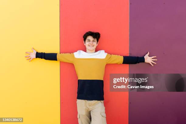 happy young man with arms outstretched against colored wall - man outstretched arms ストックフォトと画像