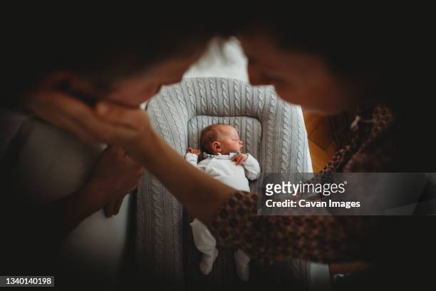 mom and dad holding hands looking at newborn baby sleeping - mum dad and baby fotografías e imágenes de stock