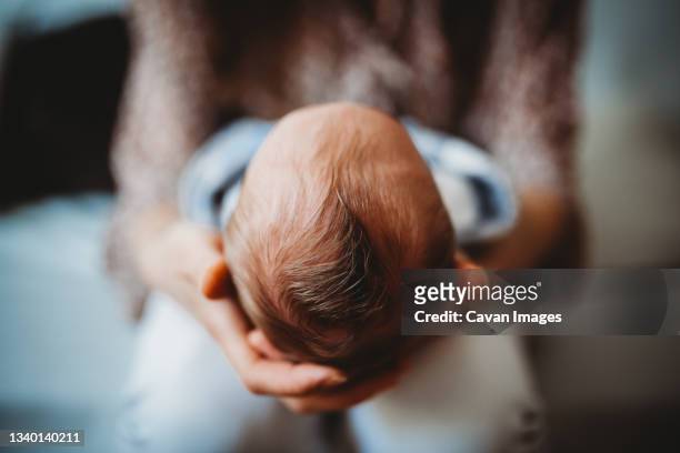 close up of mom's hands holding baby newborn head full of hair - baby touching belly fotografías e imágenes de stock