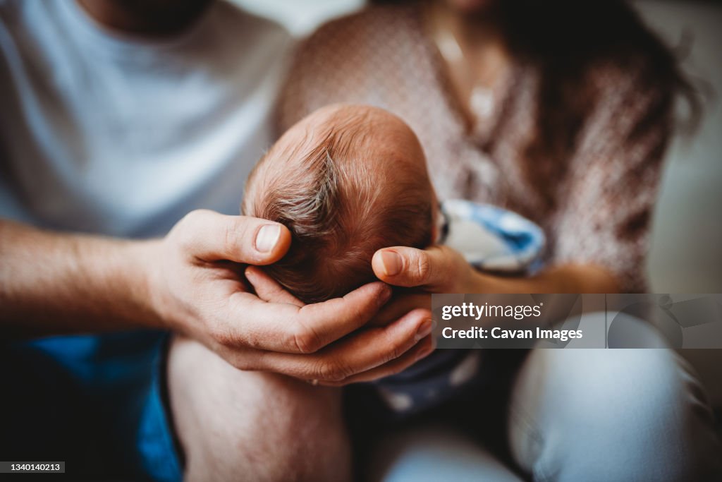 Close up of parents' hands holding baby newborn head full of hair