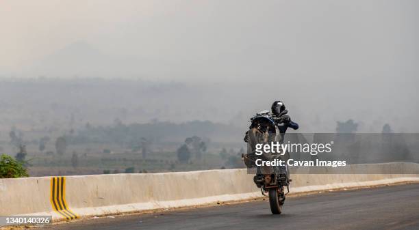 man performing wheelie on heavy adventure bike in cambodia - motorcycle stunt stock pictures, royalty-free photos & images