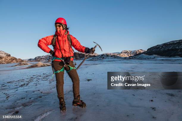 woman posing with ice pick on glacier in iceland - steigeisen stock-fotos und bilder