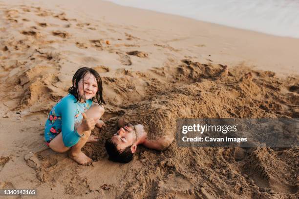 young girl gives thumbs up after burying dad in sand on waikiki beach - bury stock pictures, royalty-free photos & images