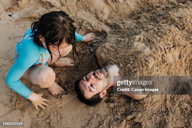 young girl buries dad in the sand on waikiki beach during sunset - bury fotografías e imágenes de stock