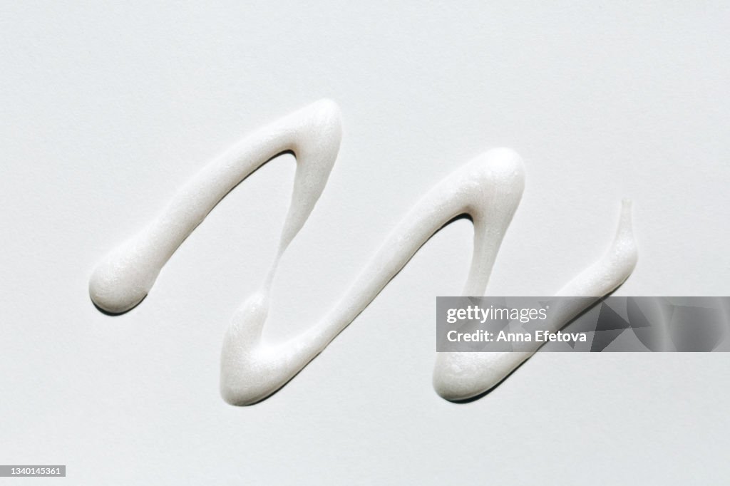 Textured smear of white highlighter with silver glittering particles. Body lotion with shimmer or sunscreen oil for perfect skin. Macrophotography in flat lay style