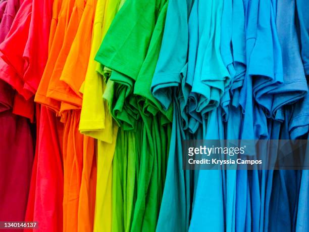 lots of bright  -rainbow colors display- t-shirts hanging on rack - slogan t shirt stock-fotos und bilder