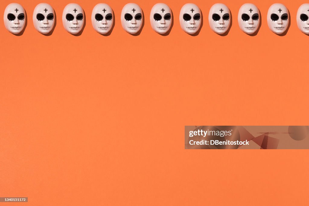 Repetitive halloween killer mask pattern with a cross on the forehead and pronounced dark circles on top line on an orange background. Halloween celebration concept.