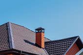 Brick chimney pipe on metal roof of a private house against the sky