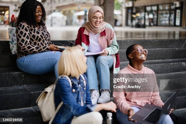 multiethnic students sit on the steps near the college and look at the laptop and  digital tablet and talk - big city life stock pictures, royalty-free photos & images