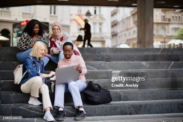 los estudiantes se sientan en los escalones cerca de la universidad y miran la computadora portátil y la tableta digital y hablan - students fotografías e imágenes de stock