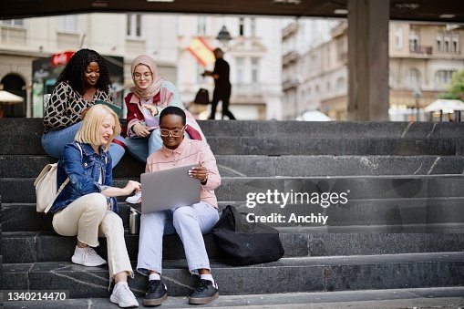 Students sit on the steps near the college and look at the laptop and digital tablet and talk Students sit on the steps near the college and look at the laptop and digital tablet and talk