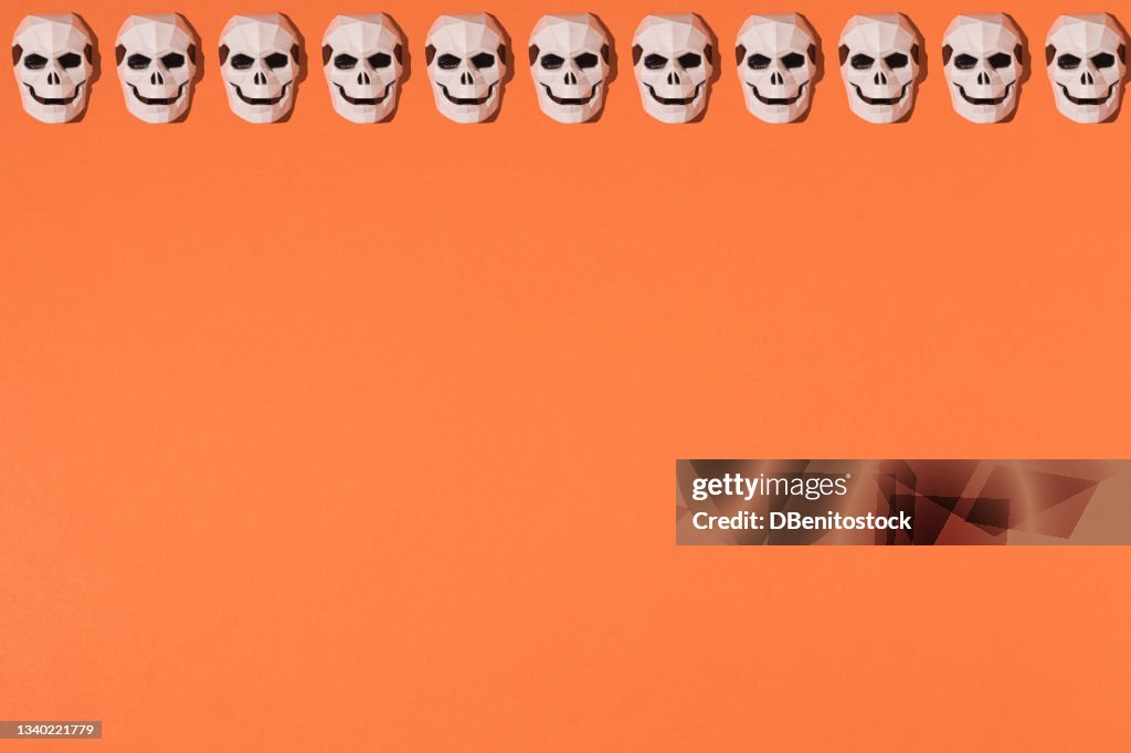 Repetitive killer skeleton mask pattern on top line on orange background. Halloween celebration concept.