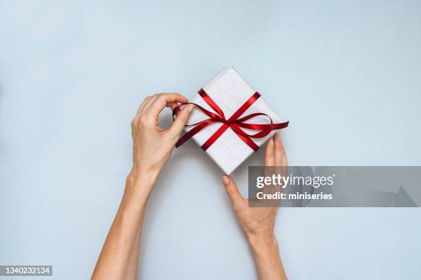 top view of female hands tied red bow on a christmas present - gift hand stock pictures, royalty-free photos & images