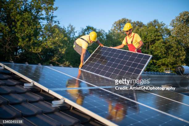 bauarbeiter installieren sonnenkollektoren auf einem dach - installieren stock-fotos und bilder