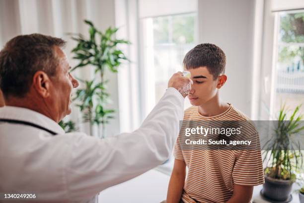 senior doctor is checking patient's temperature while nurse is taking notes in medical chart - heat illness stock pictures, royalty-free photos & images