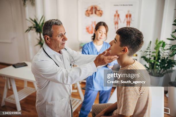 doctor is examining the patient's glands at the clinic while nurse is taking notes in medical chart - teen and doctor stock pictures, royalty-free photos & images