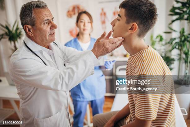 doctor is examining the patient's glands at the clinic while nurse is taking notes in medical chart - human gland stockfoto's en -beelden