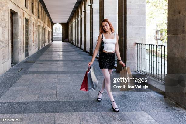 hermosa mujer caminando por la acera debajo de unos arcos en una ciudad mientras lleva unas bolsas de la compra. - personas ciudad stock pictures, royalty-free photos & images