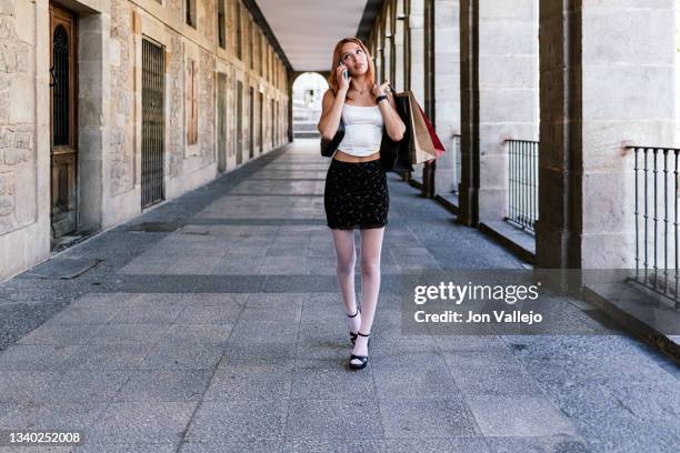 mujer joven lleva unas bolsas de la compra mientras esta hablando por el teléfono inteligente mientras compra en la ciudad - teléfono inteligente stock-fotos und bilder