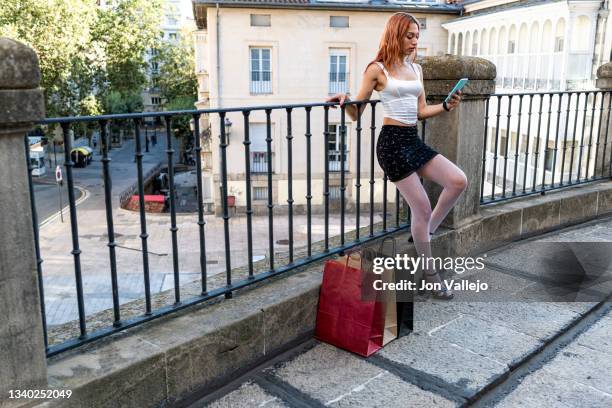 mujer pensativa con bolsas de la compra sosteniendo un teléfono inteligente en la ciudad - pensativa stock-fotos und bilder