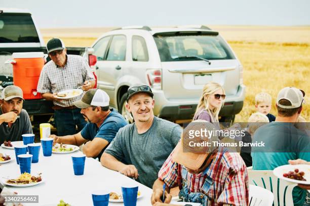 medium wide shot of farmers sharing family meal in wheat field during summer harvest - harvest table stock-fotos und bilder