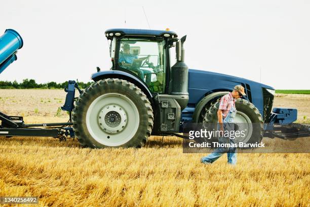 Wide shot of farmer walking past tractor in cut wheat field during harvest