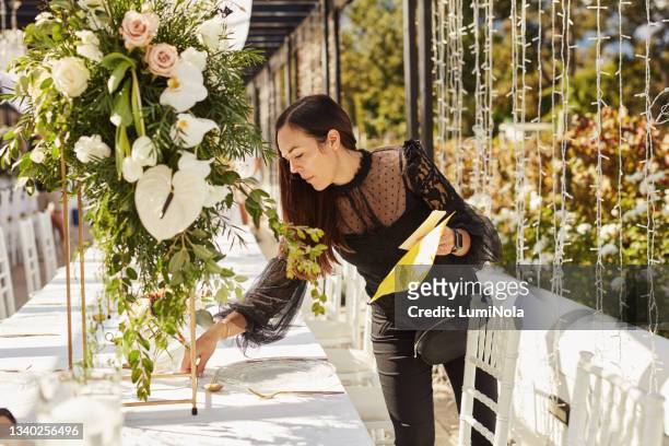 shot of a young woman decorating a table with place card holders in preparation for a wedding reception - wedding table setting stockfoto's en -beelden