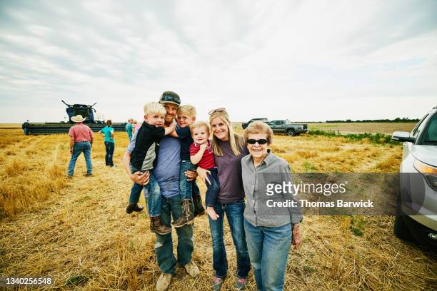 medium wide shot portrait  of smiling grandmother and family holding sons in cut wheat field during summer harvest - autobauer stock-fotos und bilder