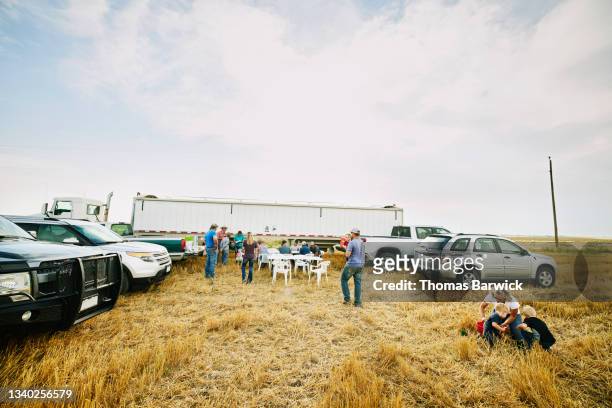 Extreme wide shot of multigenerational farm family sharing meal in wheat field during harvest
