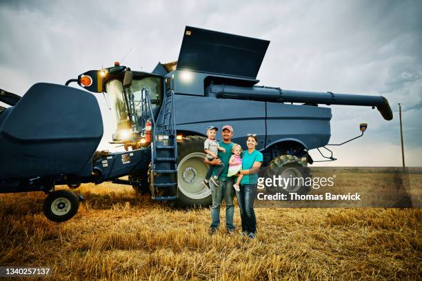 wide shot portrait of family standing in front of combine in wheat field during summer harvest - farm equipment stock pictures, royalty-free photos & images