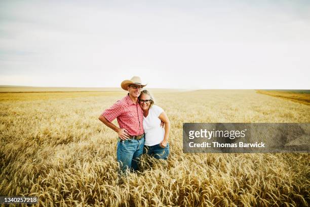Wide shot of smiling couple embracing in wheat field during summer harvest