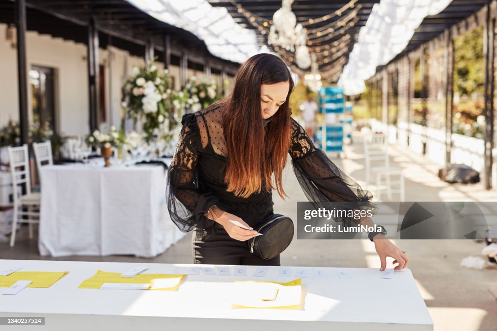 Shot of a masked young woman decorating a table with place card holders in preparation for a wedding reception