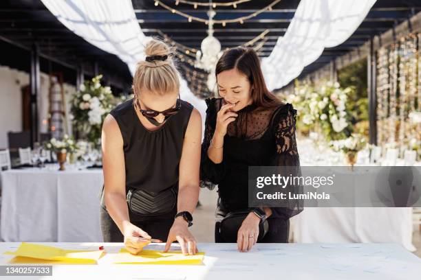 shot of two masked young women decorating a table with place card holders in preparation for a wedding reception - wedding guest list stock pictures, royalty-free photos & images