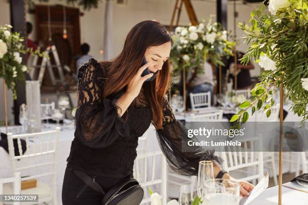 aufnahme einer jungen frau, die ein smartphone benutzt, während sie einen hochzeitsort dekoriert - wedding planner stock-fotos und bilder