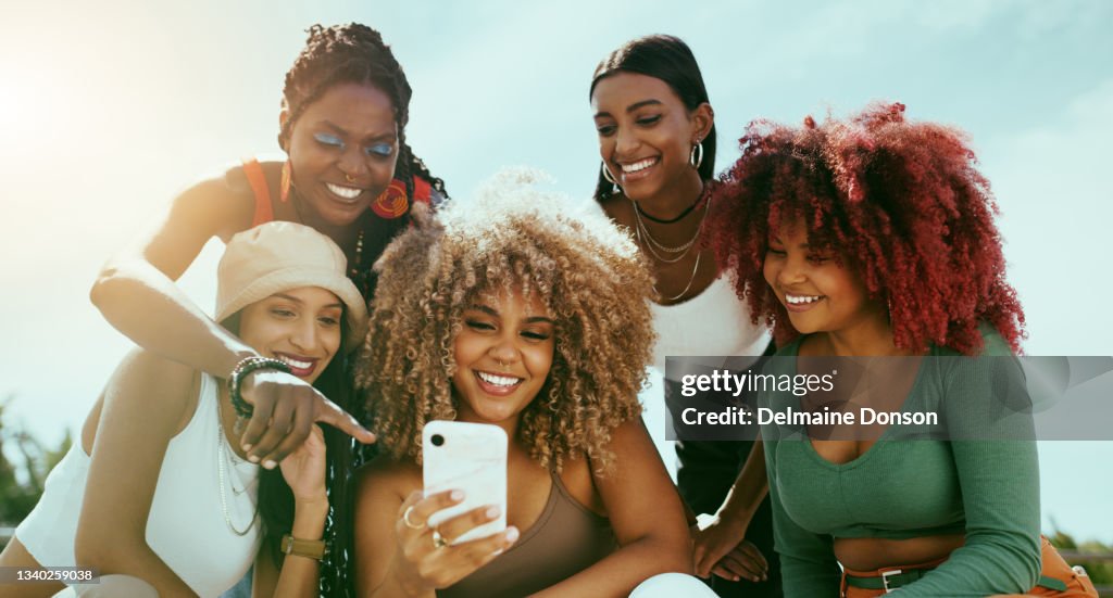 Foto de un grupo de jóvenes amigas usando un teléfono en la ciudad