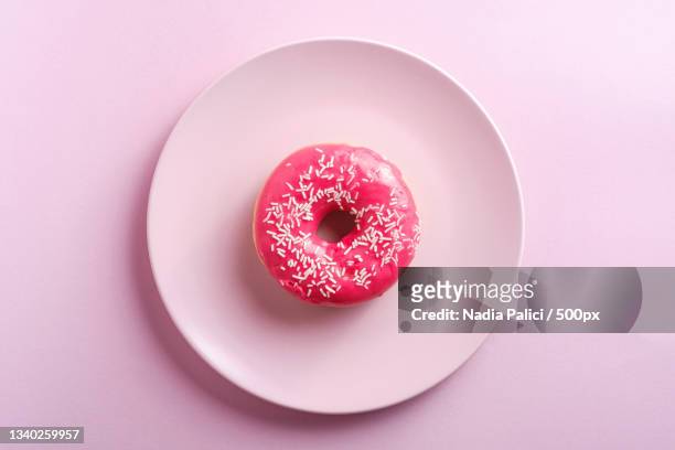 directly above shot of donut in plate on pink background - ungesund stock-fotos und bilder