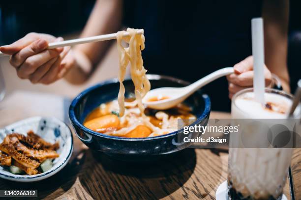 close up of young asian woman enjoying a bowl of taiwanese style beef noodle soup with appetitizer and a glass of iced bubble tea in restaurant. asian cuisine and food culture. eating out lifestyle - アジア料理 ストックフォトと画像