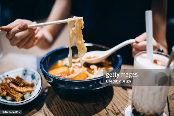 close up of young asian woman enjoying a bowl of taiwanese style beef noodle soup with appetitizer and a glass of iced bubble tea in restaurant. asian cuisine and food culture. eating out lifestyle - taiwanese ethnicity stockfoto's en -beelden