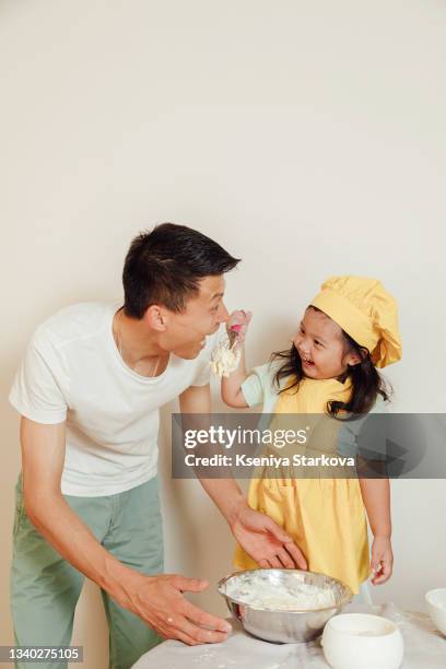 young asian daddy cooks with his little daughter in yellow apron and chef's hat - chef team stock pictures, royalty-free photos & images