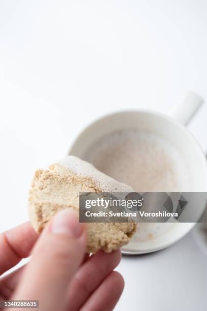 close up coffee and cookie. woman holds in fingers homemade coconut gluten free cookie which she dipped in vegan cappuccino in mug on the white background. - coconut biscuits stock pictures, royalty-free photos & images