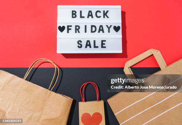 black friday in a light box and recycled paper bags on a black and red background - friday stock pictures, royalty-free photos & images