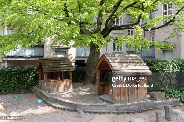 two wooden children’s playhouses in the shade of a big tree with springtime green leaves - courtyard stockfoto's en -beelden